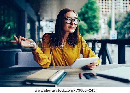 Half length portrait of pretty redhead businesswoman dressed in stylish clothing gesturing and thinking about creative ideas for startup project while making research on digital tablet outdoors
