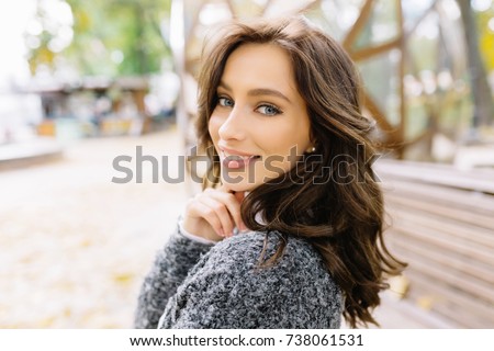 Close up portrait of sensitive woman is turn around at camera and smiles. She has dark short hair and wonderful big blue eyes. She is playfully looks at the camera. Background green park.