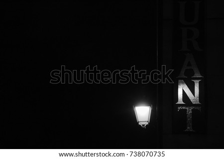 Restaurant sign (seen partially) illuminated by old street lantern at evening. Black and white photo.