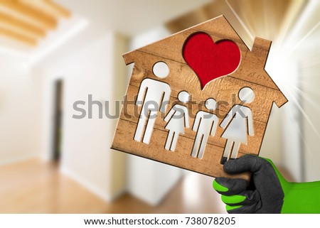 Interior design concept - Hand with work glove holding a wooden model house with a family and heart in a living room