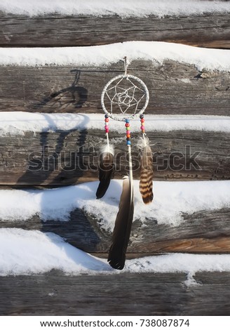 Dream catcher on old wooden snow covered wall background. Homemade decor with beads and feathers.