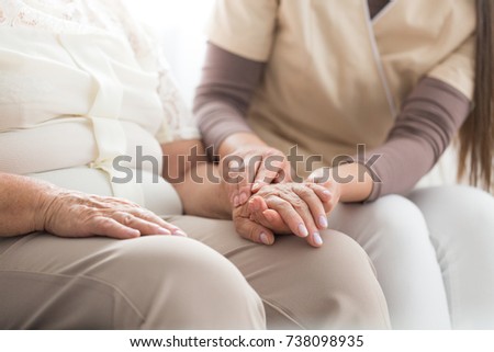 Close-up of nurse taking care about elderly person with parkinson while sitting together at home