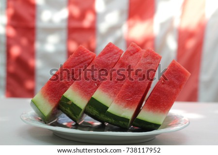 Watermelon slices in front of United States flag, outside at a summer barbecue, as for Memorial Day or the Fourth of July / Independence Day. Royalty-Free Stock Photo #738117952