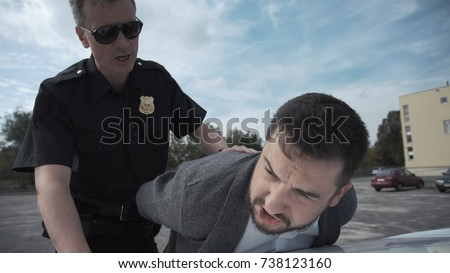 Police officer arresting criminal, putting him on car trunk and reading rights for him. Royalty-Free Stock Photo #738123160