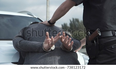 Police officer arresting criminal, putting him on car trunk and reading rights for him. Royalty-Free Stock Photo #738123172