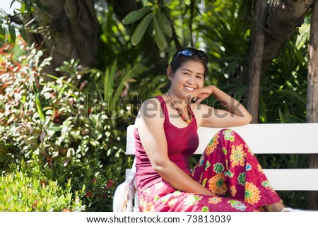 Exterior view of a middle aged woman sitting on a bench in the park