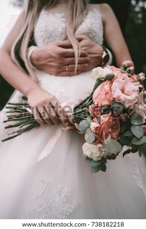 The bridegroom embraces the bride's waist, a wedding bouquet in her hands, in focus a bouquet