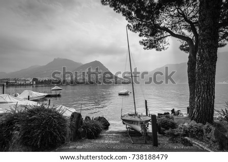 Boats and trees on Lake Lugano, mountain Monte Bre in the background. Black and white photography.