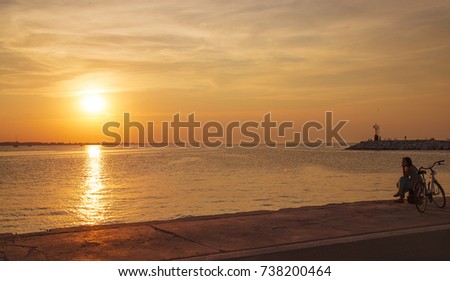 Girl with bicycle on the pier at sunset.