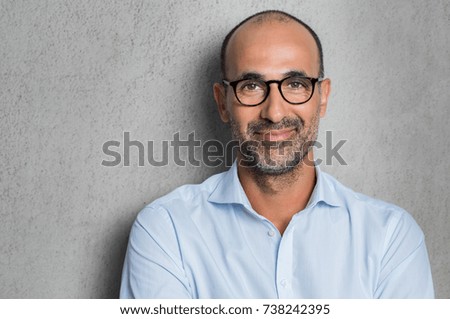 Portrait of a mature businessman wearing glasses on grey background. Happy senior latin man looking at camera isolated over grey wall with copy space. Close up face of happy successful business man. Royalty-Free Stock Photo #738242395