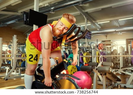 A fat man is tired on a simulator in the gym Royalty-Free Stock Photo #738256744