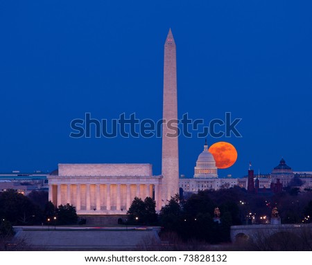 Large full moon rises through the haze over the Capitol building in Washington DC with Lincoln Memorial and Washington Monument aligned