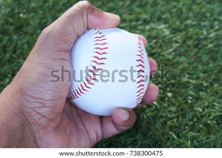 A hand holding the baseball with artificial grass on the background.