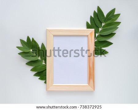 Empty wooden photo frame mock-up with green leaves around, isolated on white background