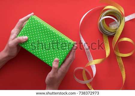 The process of wrapping and packaging Christmas and New Year gifts. Boxes, ribbons on a red background with female hands holding a box. Flat lay, top view