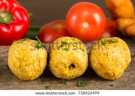 Bolon, an ecuadorian typical food with a blurred tomato and pepper behind, over a wooden table Royalty-Free Stock Photo #738426499