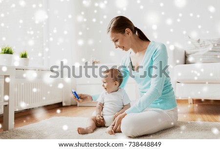 family, technology, child and parenthood concept - happy smiling young mother showing smartphone to little baby at home over snow