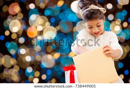 holidays, childhood and people concept - smiling little girl opening gift box over lights background