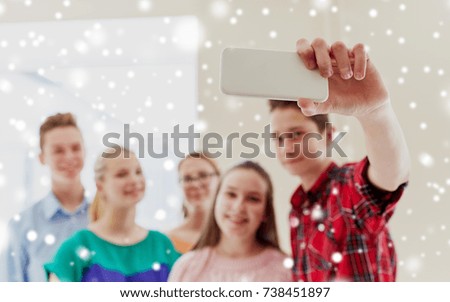 education, school, technology and people concept - group of happy smiling students taking selfie with smartphone in corridor over snow