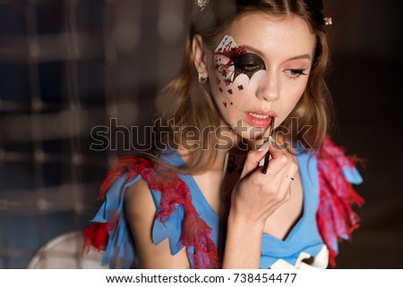 Young beautiful woman in a costume queen of hearts paints lips in red. Halloween. Costume party