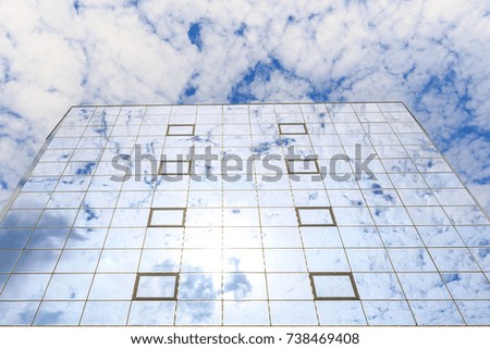 Blue clouds are reflected in the glasses of windows of a modern building. Bottom view