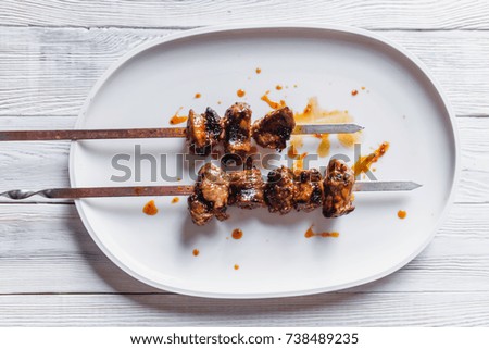 stock photo grilled meat on metal sticks over white plate with sauce