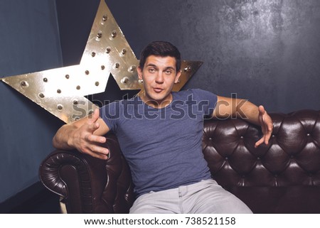 young sporty male brunette with big muscles sitting on a leather sofa near the scenery in the shape of a star with lights and actively talking to customers.sitting on a leather sofa.emotional portrait