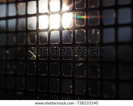 Macro close up blurred black iron mosquito wire screen under morning sun ray reflection, abstract background, dark front view with bright round sun shining on top