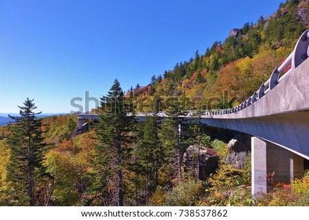 Unique & beautiful view of the Blue Ridge Parkway's Linn Cove Viaduct on a nice autumn day & trees with fall colors under a clear blue sky. Photo taken snuggled up to side of viaduct at ground level.