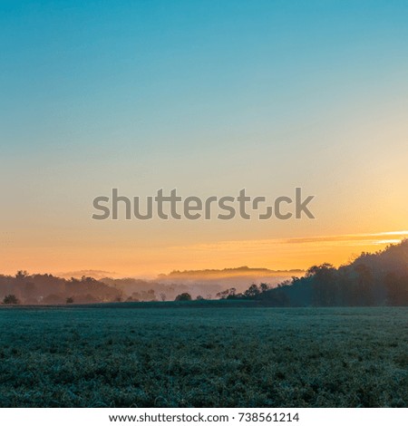 Square image of misty sunrise with field and hills
