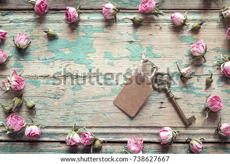 Vintage key with a tag and a little pink roses on an old wooden background. Place for text.