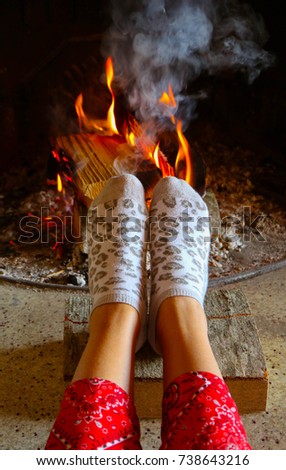 Burning wood at the fireplace, female legs in socks warming up. Firewood bricks at the fire, woman foot heating. 