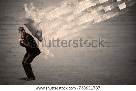 Business man protecting with umbrella against wind of papers concept