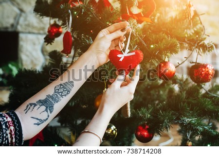 The girl hangs on the Christmas tree toy in the shape of a heart.