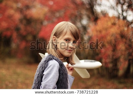 Happy funny child with aircraft. Girl is wearing funny hat and enjoying autumn and life. Kid playing on the nature outdoors.