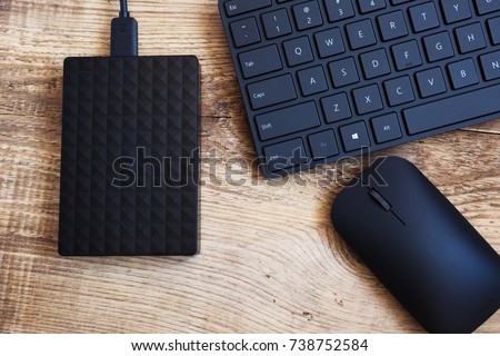 stylish black wireless keyboard, mouse  and external hard disc drive on a wooden surface