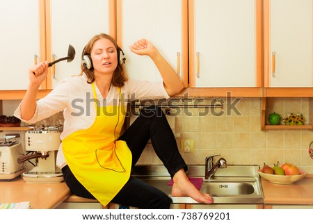 Relax in kitchen. Listening music singing and dancing. Funny happy housewife cook chef with earphones wearing yellow apron sitting and relaxing at home.