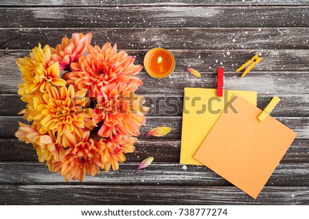 Autumn background with orange chrysanthemum on rustic wooden table. Empty notes and lit candle
