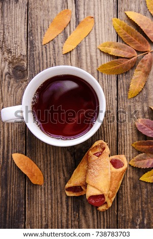 Beautiful autumn picture with yellow, red and orange leaves, a cup of tea, a scarf and a piece of paper with pen on wooden background with cookies