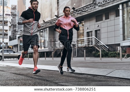 Out for a run. Full length of young couple in sport clothing running through the city street together Royalty-Free Stock Photo #738806251