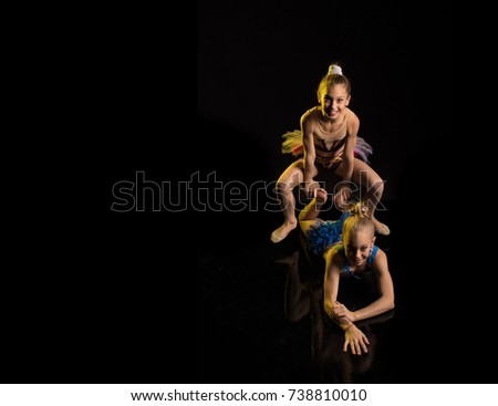 Two girls gymnasts athlete performs acrobatic elements on a black background in a yellow scenic light.