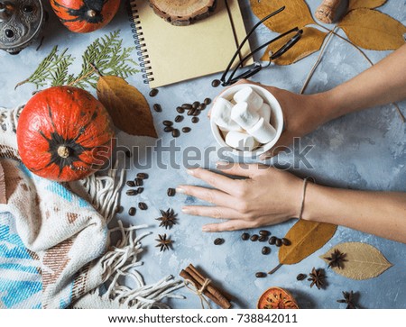 Autumn background with cup of marshmallow, yellow maple leaves and pumpkins. women's hands hold a cup. Top view