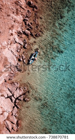 Aerial drone, bird's eye view of kayak docked in rocky island with turquoise and sapphire calm waters
