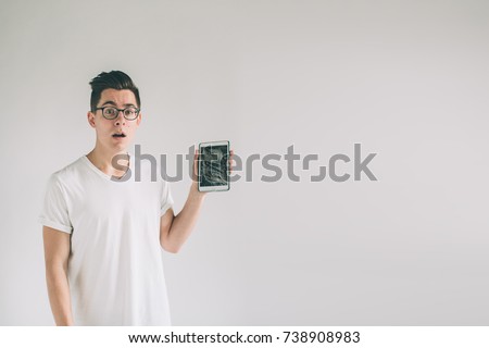 Nerd is wearing glasses. Student presenting a broken black tablet behind glass. upset man holds a out-of-use tablet or smartphone. Isolated on a light background. Broken screen