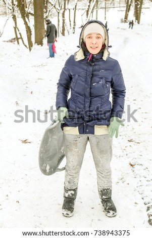 Beautiful caucasian girl laughing and having fun riding a saucer sled downhill in a forest or city park.  Showing her resent after  the pants got dirty after downhill.
