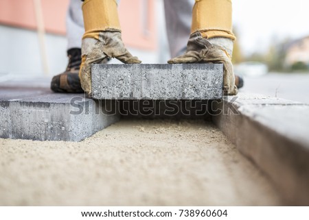 Close up of the gloved hands of a builder laying outdoor paving slabs on a prepared base. Royalty-Free Stock Photo #738960604