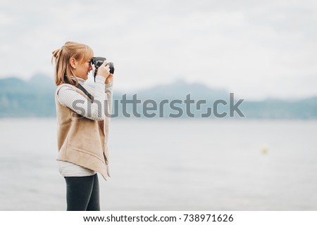 Cute little preteen girl enjoying nice day on lake Geneva, taking pictures with dslr camera, wearing beige jacket. Travel with children. Image taken in Lausanne; Switzerland