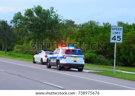 Police truck suv vehicle with flashing red and blue lights has pulled over a sports car for speeding and they happen to be on the side of the road by a speed limit sign. Royalty-Free Stock Photo #738975676