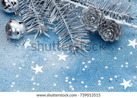 silver christmas tree branches with cones and jingle bells. sparkling stars on blue background.