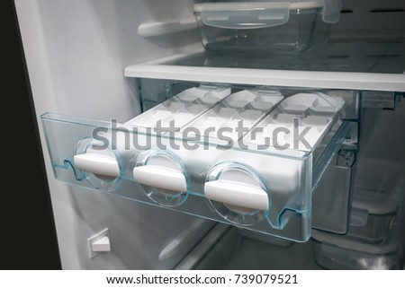 Closed up white side by side ice maker and ice tray in new open freezer.